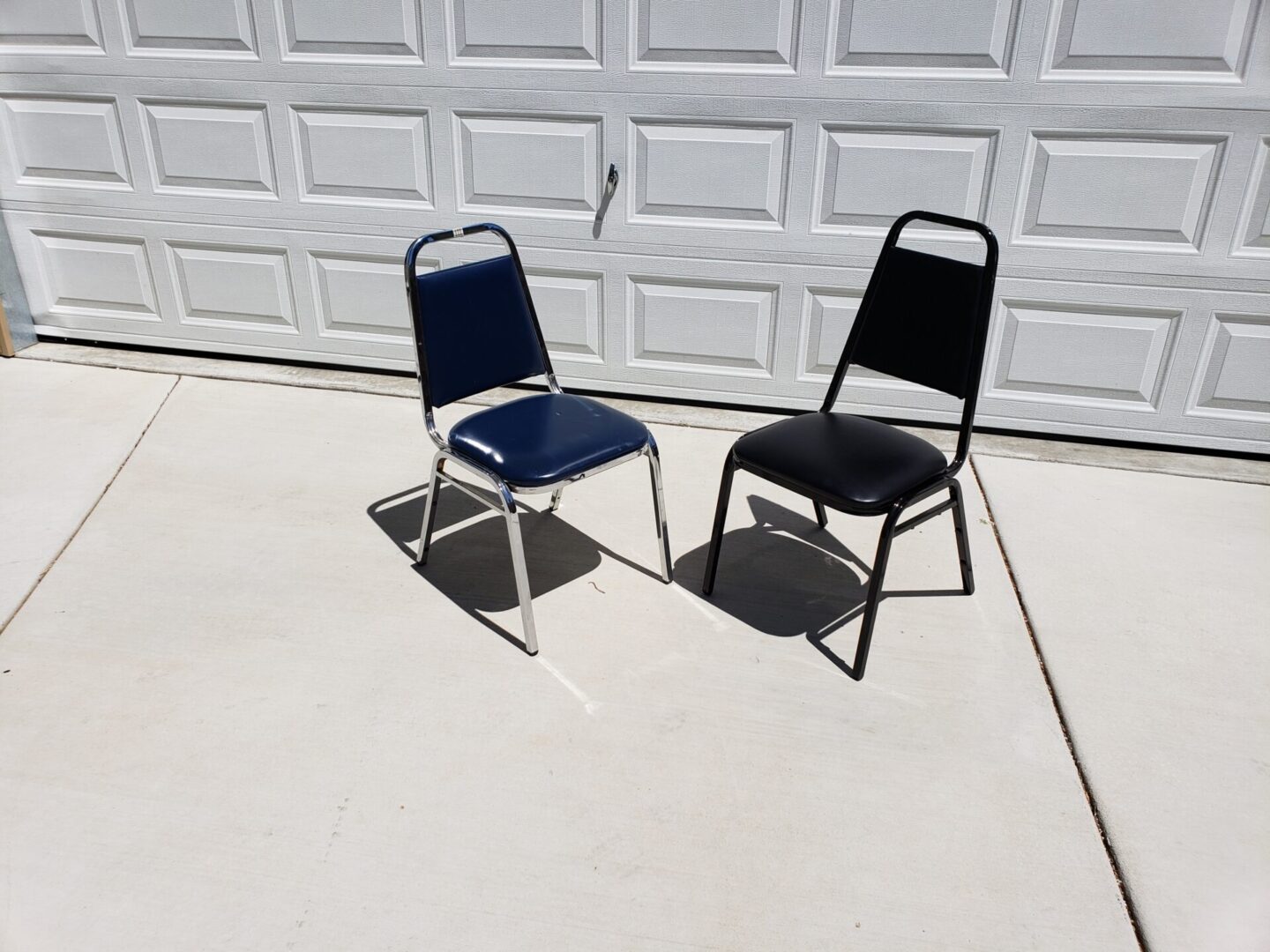Two folding chairs, one blue and one black, sitting on concrete.