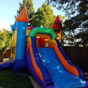 Colorful inflatable bounce house with a slide in a backyard.