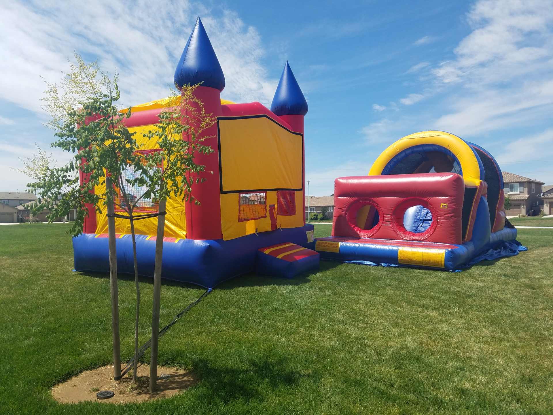 Colorful inflatable bounce house and slide set up on green grass under a clear sky.